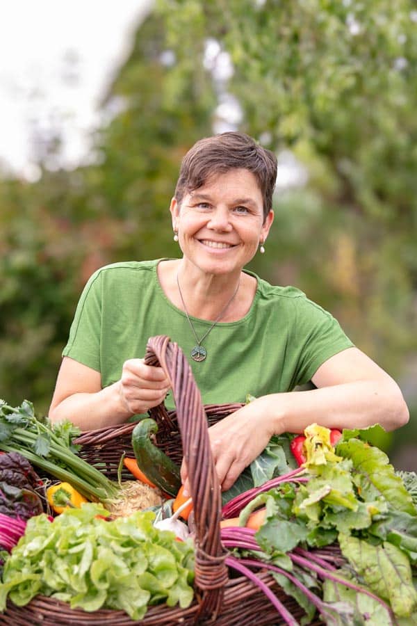 ASG_3012 Kopie Katrin SchĂ€fer â ErnĂ€hrungstherapeutin & Coachin hĂ€lt einen Korb in den HĂ€nden mit GemĂŒse aus dem Garten